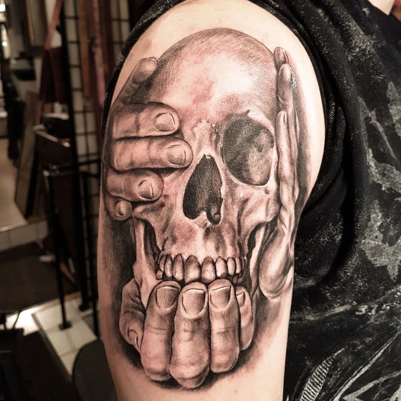 Photorealistic upper arm tattoo – skull held by two hands, black and grey realism, Evgenij Korsun, Tattoo Jaga Wiesbaden